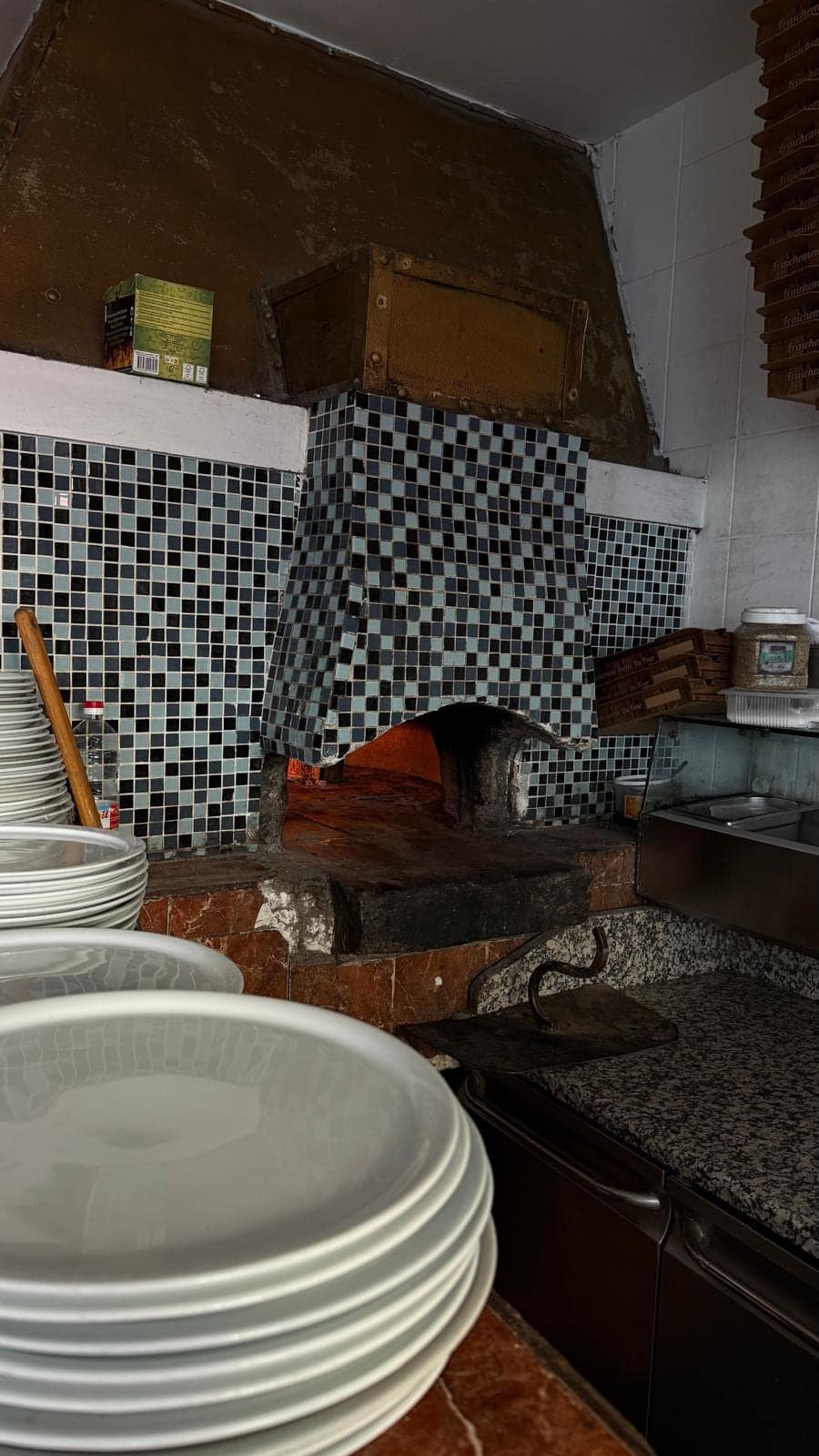 Le four à bois allumé, carrelé de mosaïque noire et blanche, et les piles d’assiettes du pizzaiolo.