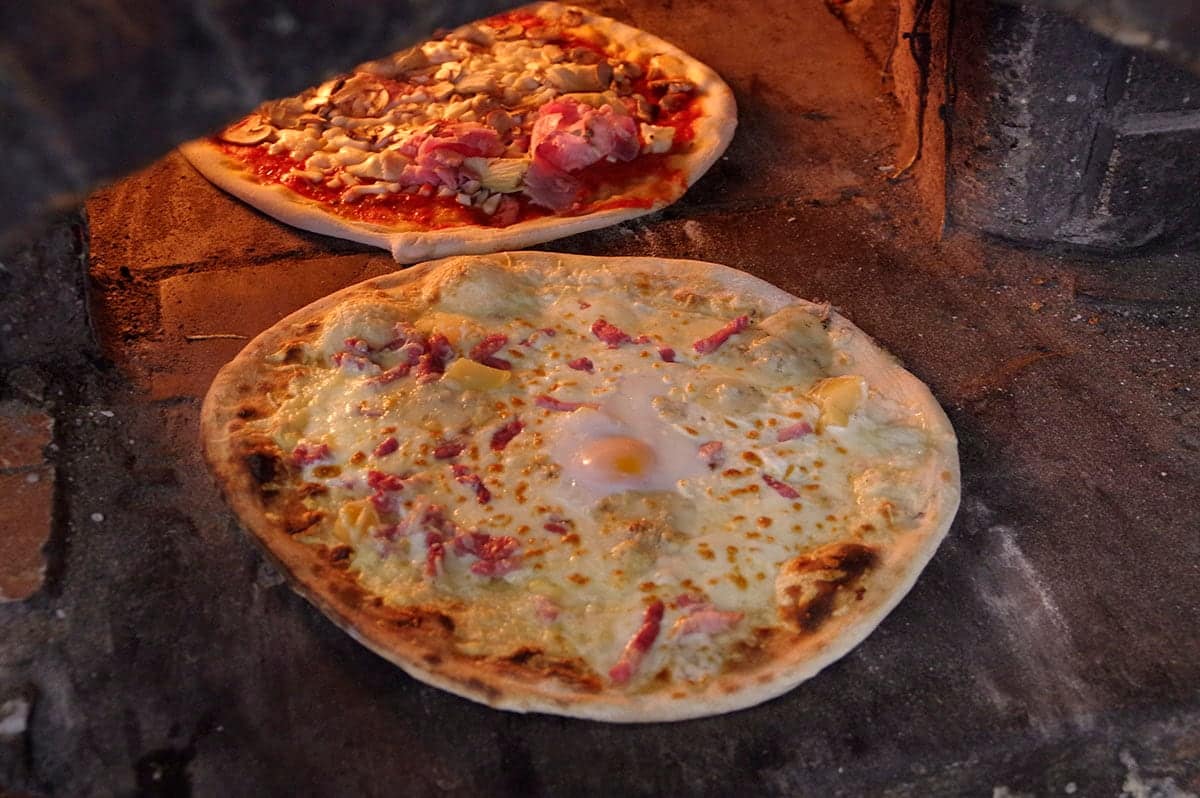 Deux pizzas à pâte fine en train de cuire sur la sole du four à bois.