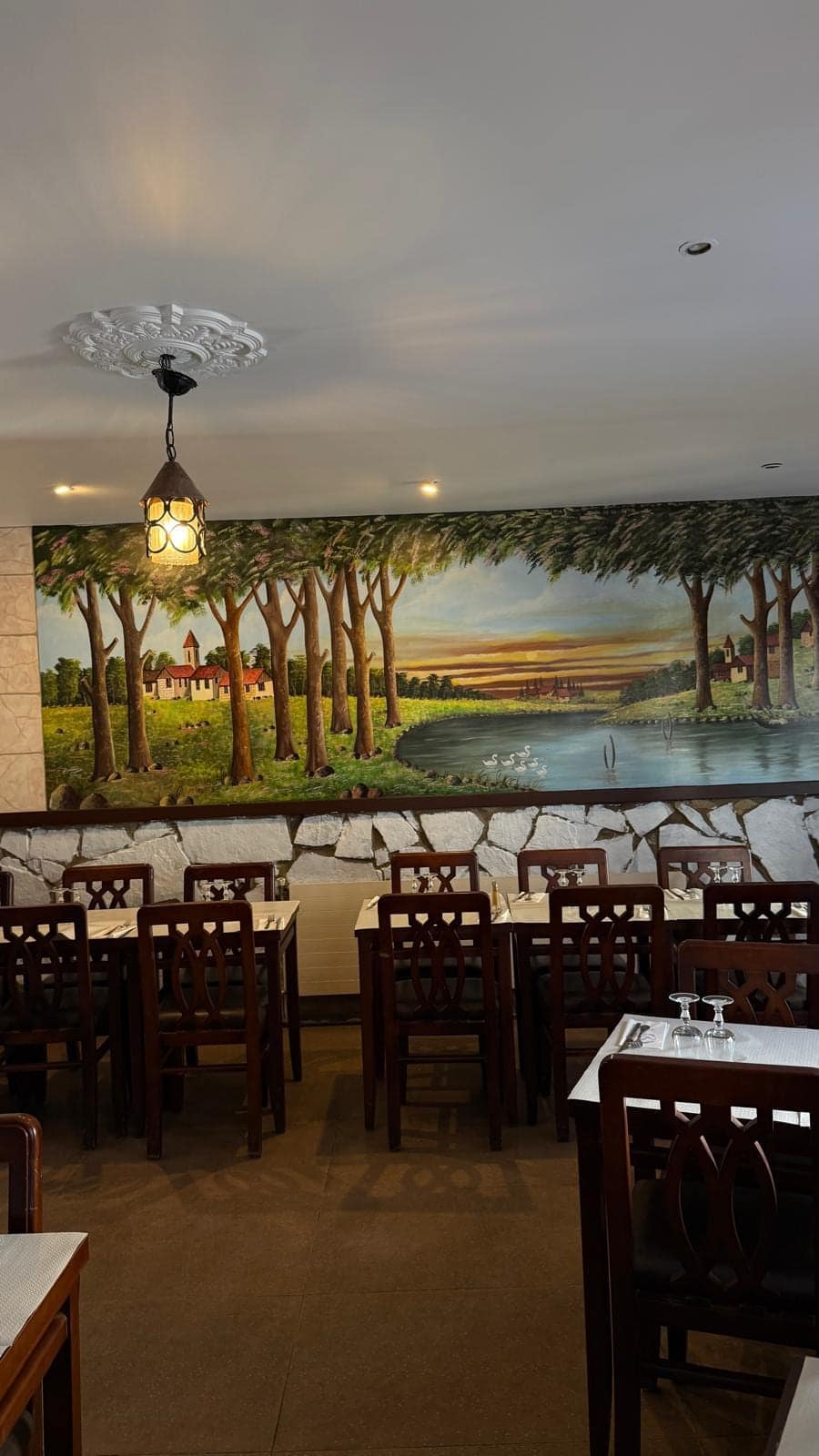 La fresque d’un paysage d’arbres au soleil couchant, au-dessus des tables de la salle.