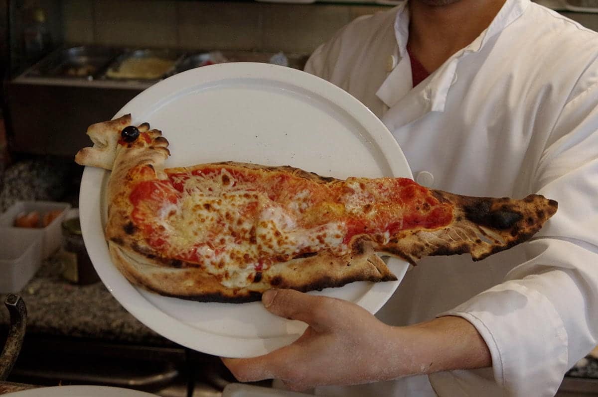 Une pizza façonnée en forme de poisson, présentée sur assiette par le pizzaiolo.