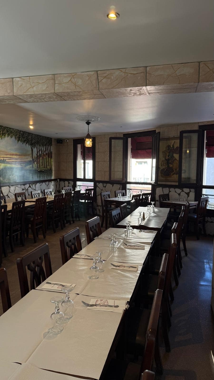 La salle vue du fond : longues tables dressées, fresque et fenêtres sur rue.