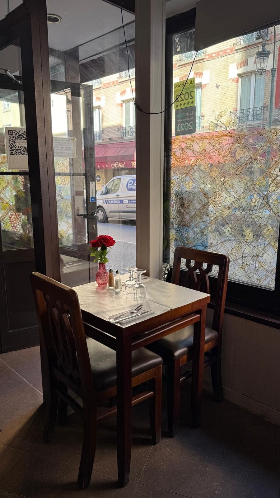 Table pour deux près de la vitrine, une rose rouge sur la nappe blanche.
