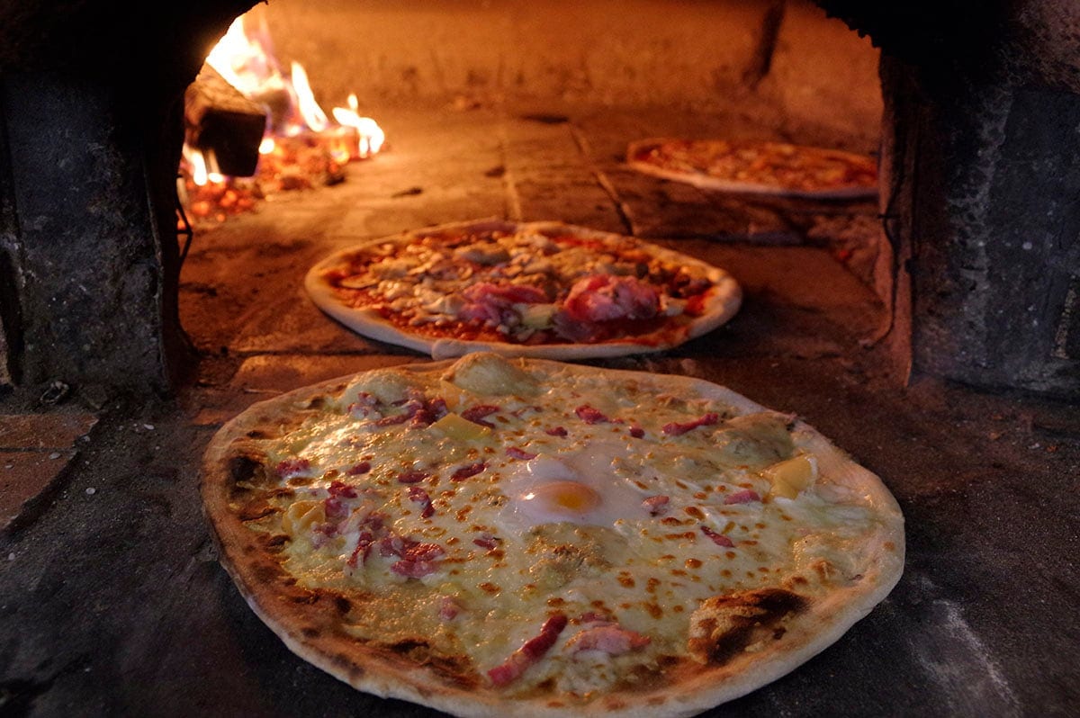 Pizzas en cuisson dans le four, devant le feu de bois.