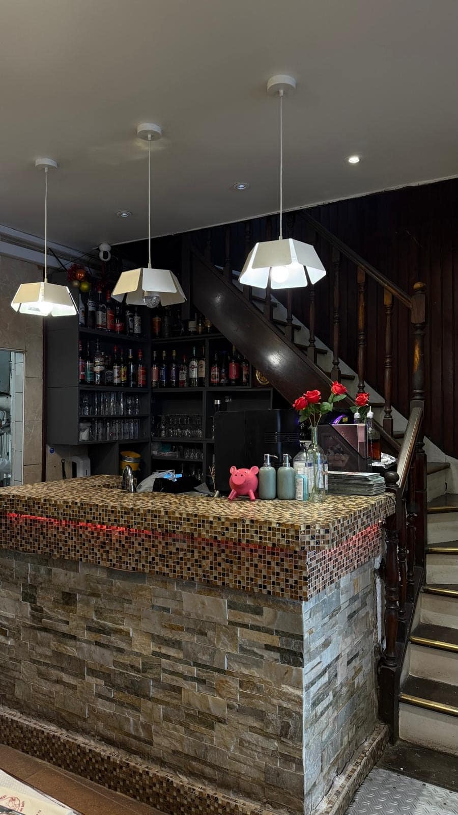 Le comptoir en pierre et mosaïque, les bouteilles du bar et l’escalier en bois.