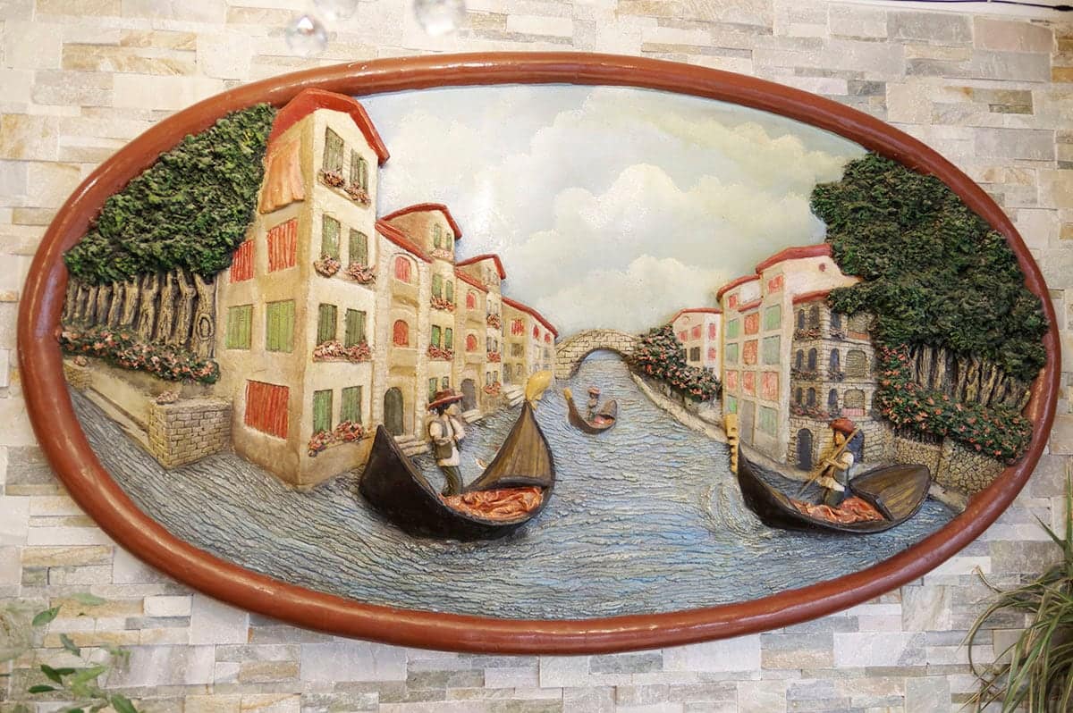 Bas-relief ovale peint d’un canal de Venise, gondoles et façades colorées.