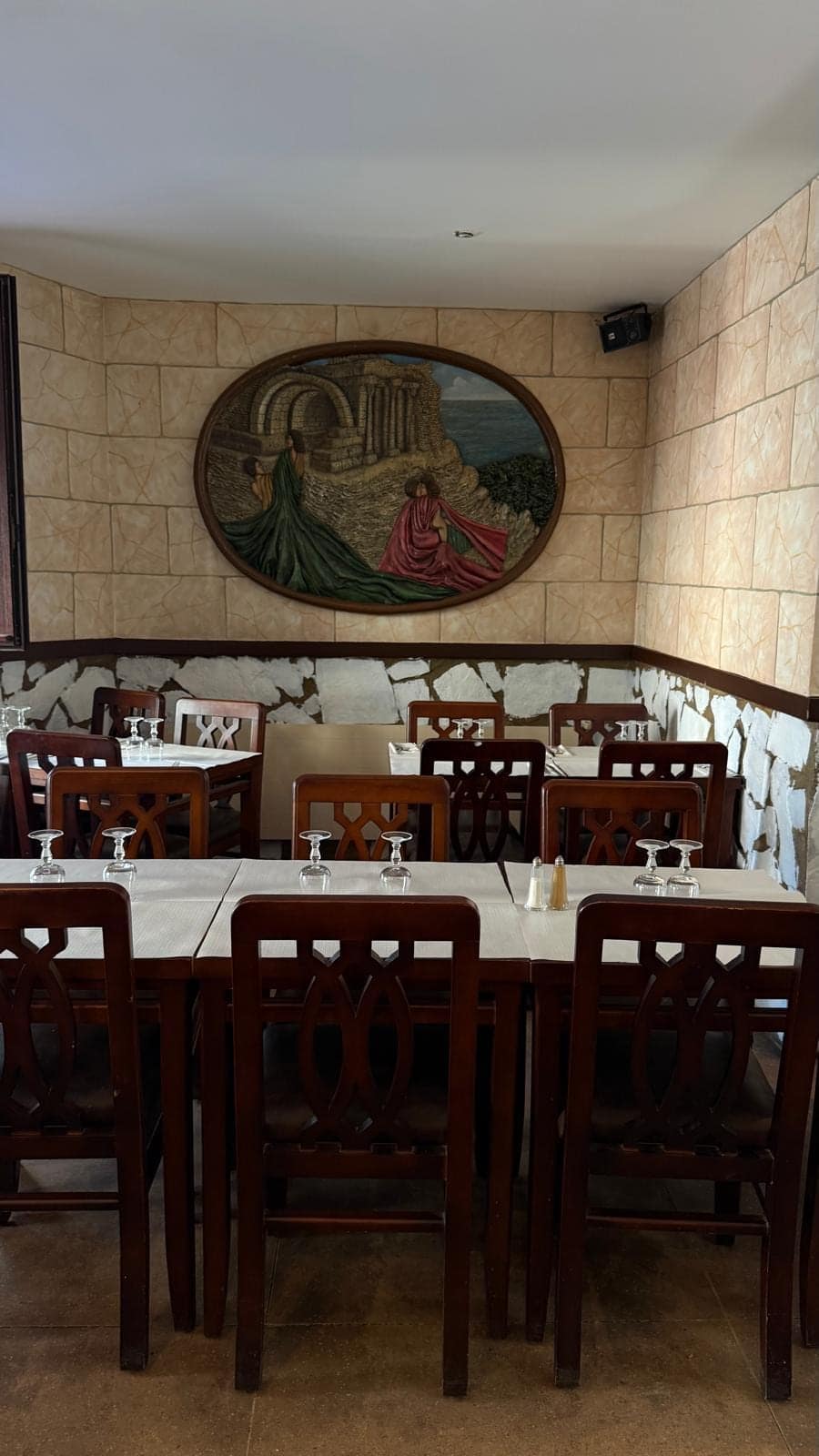 Tables et chaises en bois sombre sous le bas-relief ovale aux deux figures drapées.