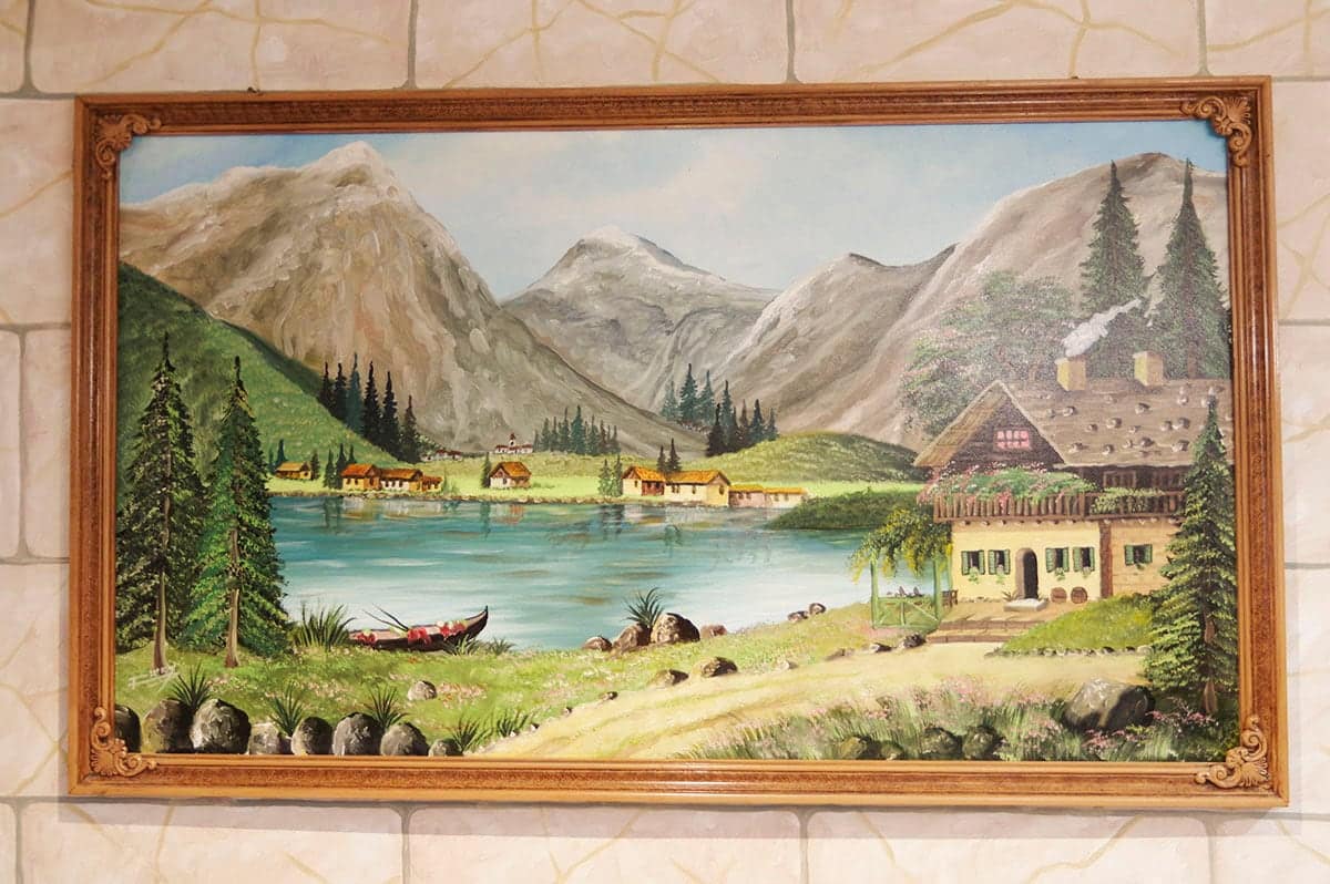 Tableau encadré d’un lac de montagne et de son chalet, sur le mur de pierre claire.
